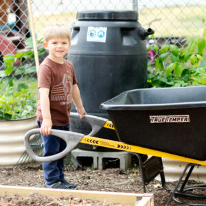 Head Start Young boy carries a wheelbarrow in a garden.